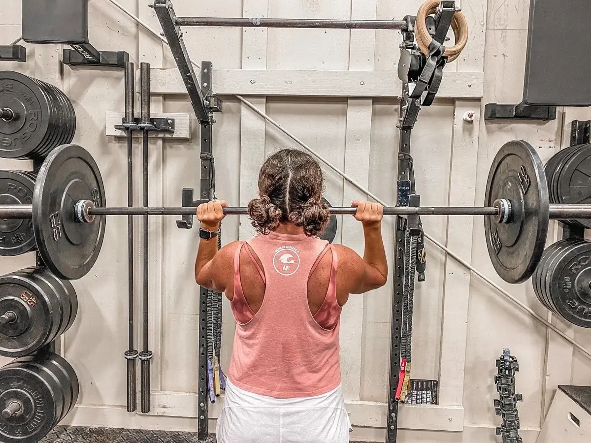 A member in a Momentum Fitness tank setting up a back squat at the rack